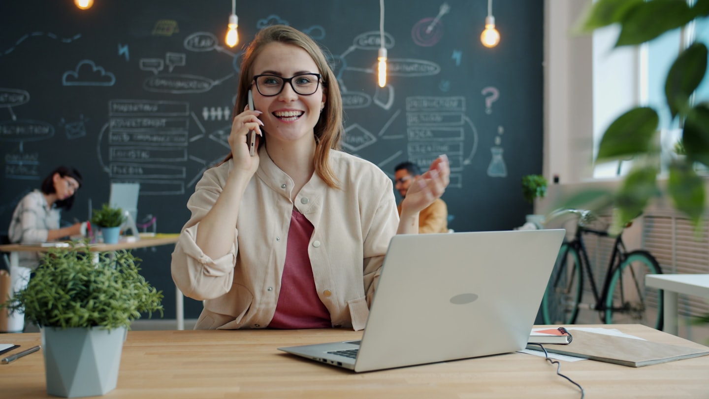 Woman with glasses talks on phone in a modern office.