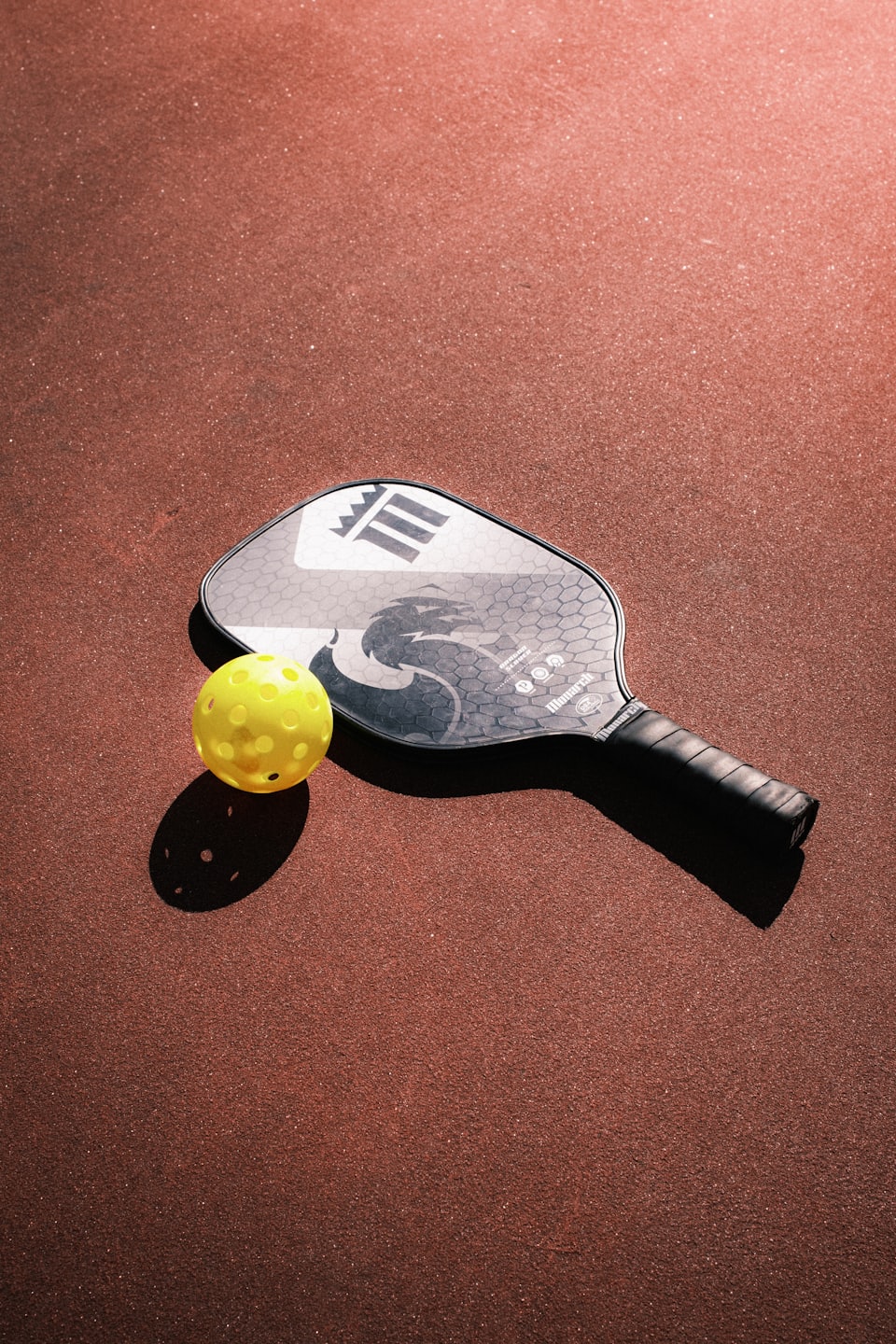 Pickleball paddle and ball on a granular court.