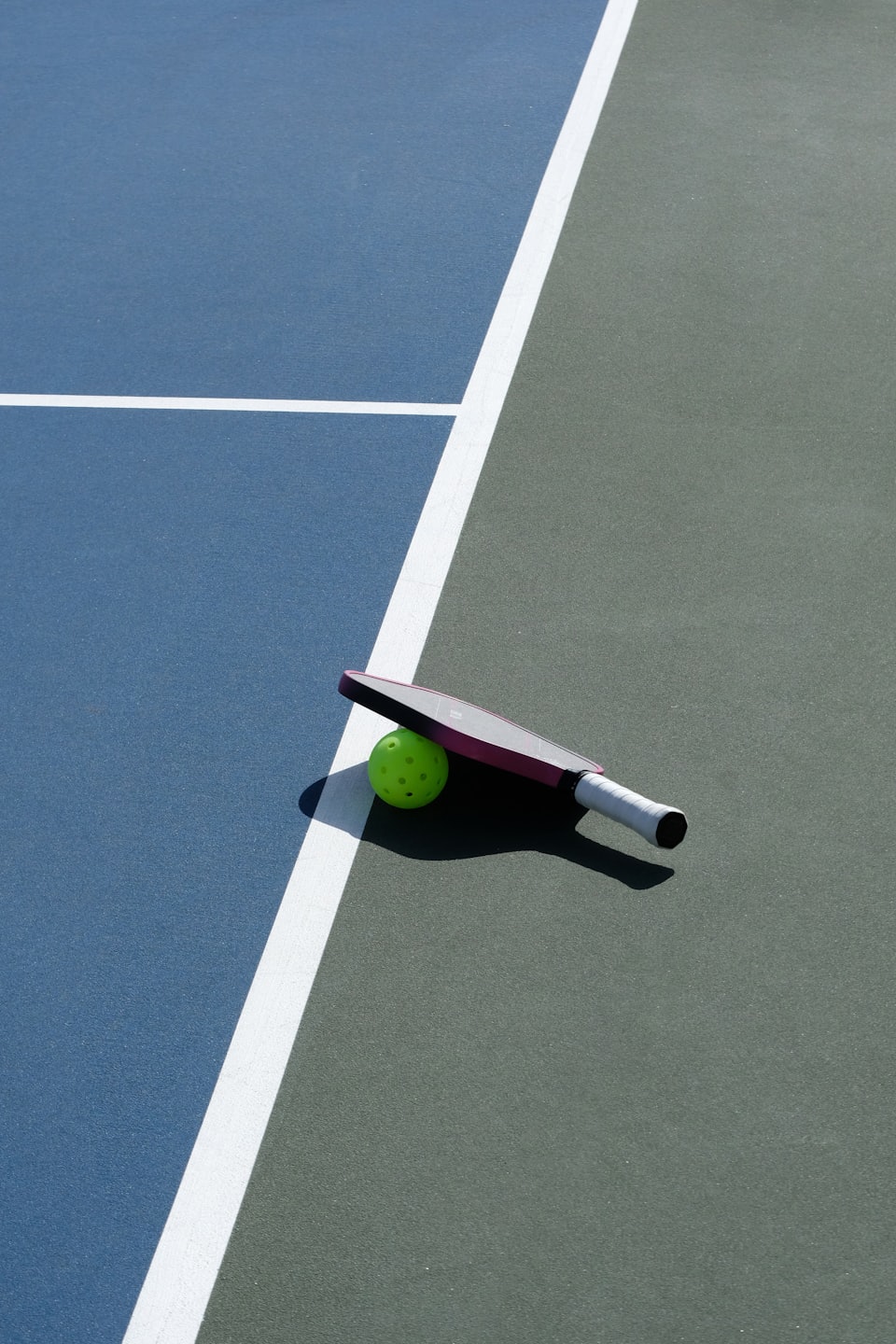 Pink and white pickleball paddle resting on a green ball.